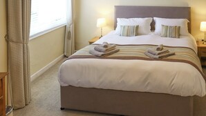 A neatly made bed with pillows and folded towels, a bedside lamp, and a window with curtains. - 2 bedroom accommodation in Freshwater East near Pembroke (Freshwater East near Pembroke)