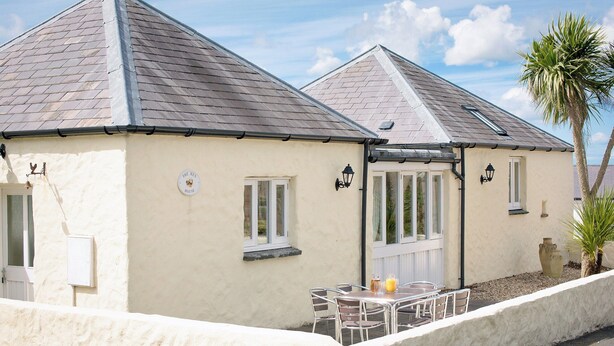 A two-story building with a tiled roof, a white exterior, and a small patio area with a table and chairs. - 2 bedroom accommodation in Freshwater East near Pembroke (Freshwater East near Pembroke)