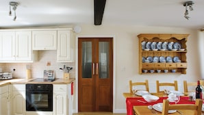 A kitchen with white cabinets, a wooden dining table set with plates and glasses, and a shelf with blue and white dishes. - 2 bedroom accommodation in Freshwater East near Pembroke (Freshwater East near Pembroke)