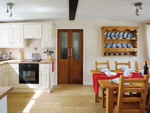 Une cuisine avec des meubles blancs, une table à manger en bois mise avec des assiettes et des verres, et une étagère avec de la vaisselle bleue et blanche.