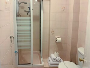 Un baño con cabina de ducha de vidrio, inodoro y un perchero con toallas.