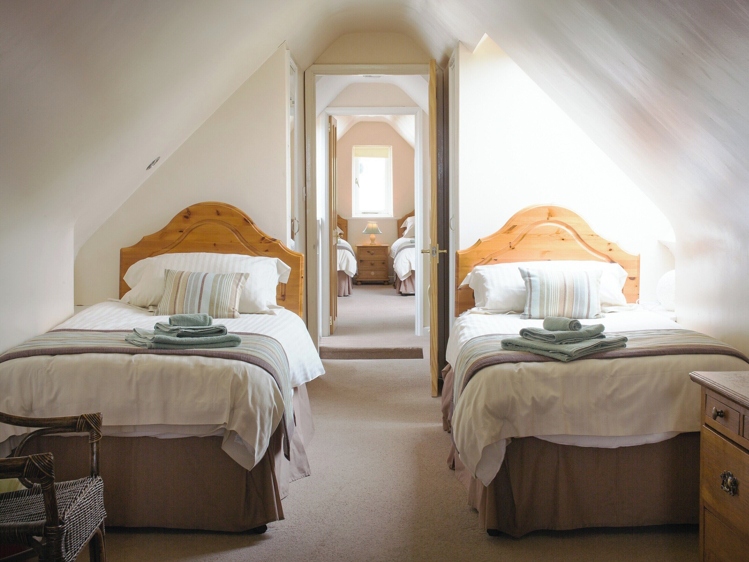 A bedroom with two beds, each with a wooden headboard, a chair, and a dresser.