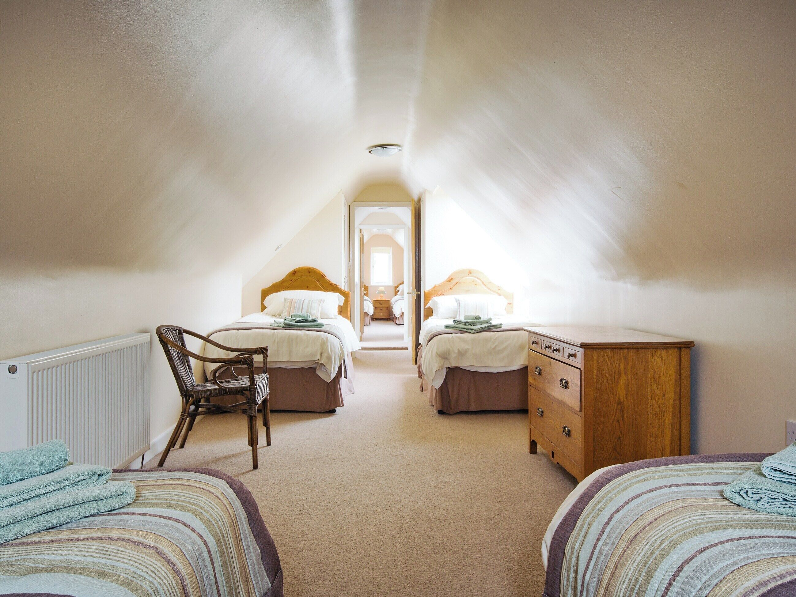A cozy attic bedroom with two beds, a wooden dresser, and a chair.