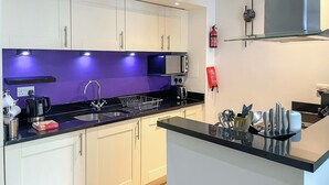 A modern kitchen with white cabinets, a black countertop, a microwave, a sink, and a fire extinguisher. - Abbey Church 14 - UKC5423 (Fort Augustus)