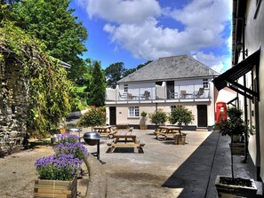 A courtyard with outdoor seating, a stone wall, and a building with a balcony. - Number Three - UKC4965 (Tawstock, near Barnstaple)