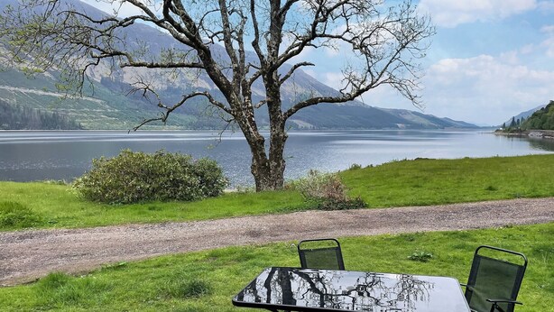 Una mesa y sillas en un patio con vistas a un lago y montañas.