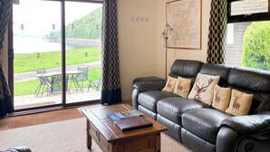 Una sala de estar con un sofá de cuero, una mesa de centro de madera y vistas a un lago a través de puertas de vidrio grandes.