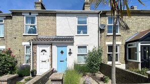 A two-story residential building with a blue door, numbered 18, and a small garden area with plants and a brick wall. - 2 bedroom accommodation in Pakefield (Pakefield)
