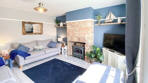 A living room with a sofa, a fireplace, a television, and a blue accent wall. - 2 bedroom accommodation in Pakefield (Pakefield)