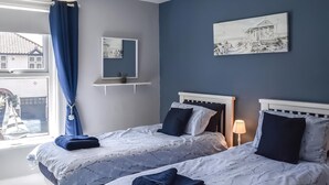 A bedroom with two beds, a window with curtains, a bedside lamp, and artwork on the wall. - 2 bedroom accommodation in Pakefield (Pakefield)