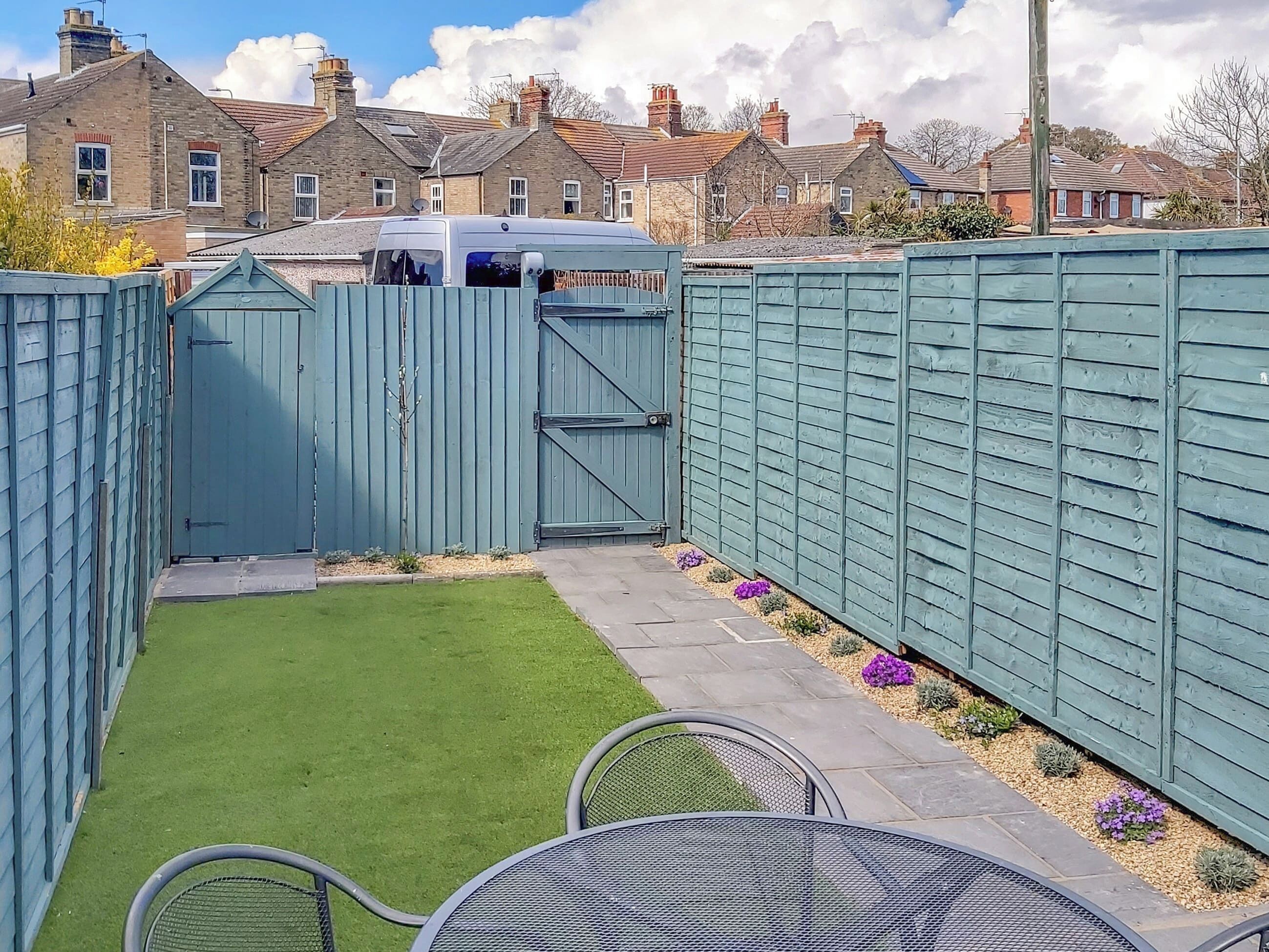 A fenced backyard with a green lawn and a patio area with metal chairs.