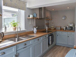 A modern kitchen with light blue cabinets, a wooden countertop, stainless steel appliances, and a window with a view. - 1 bedroom accommodation in Pakefield (Pakefield)