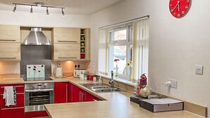 Une cuisine moderne avec des armoires rouges, une hotte de cuisinière en acier inoxydable, un four encastré, un évier et une fenêtre donnant sur l’extérieur.