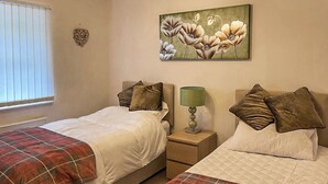 Une chambre à coucher avec deux lits, chacun recouvert d’une couverture à carreaux et agrémenté d’oreillers, une table de chevet avec une lampe, et un tableau floral accroché au mur.