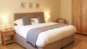 Uma cama bem arrumada com um cobertor cinza, duas mesas de cabeceira com abajures, um guarda-roupa de madeira e três quadros na parede.