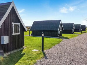A row of small, dark wooden cabins with pitched roofs, arranged on a gravel path with green grass in between. - A simply stunning eco-Pod for a fantastic getaway. (Brodie, near Forres)