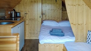 Una cabaña de madera acogedora con kitchenette, una cama y toallas dobladas con cuidado, además de un baño pequeño.