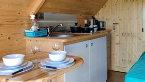 Eine kleine Küche mit Spüle, Herd und Schränken, ein Esstisch mit Schüsseln und Gläsern sowie eine Holzbalkendecke.