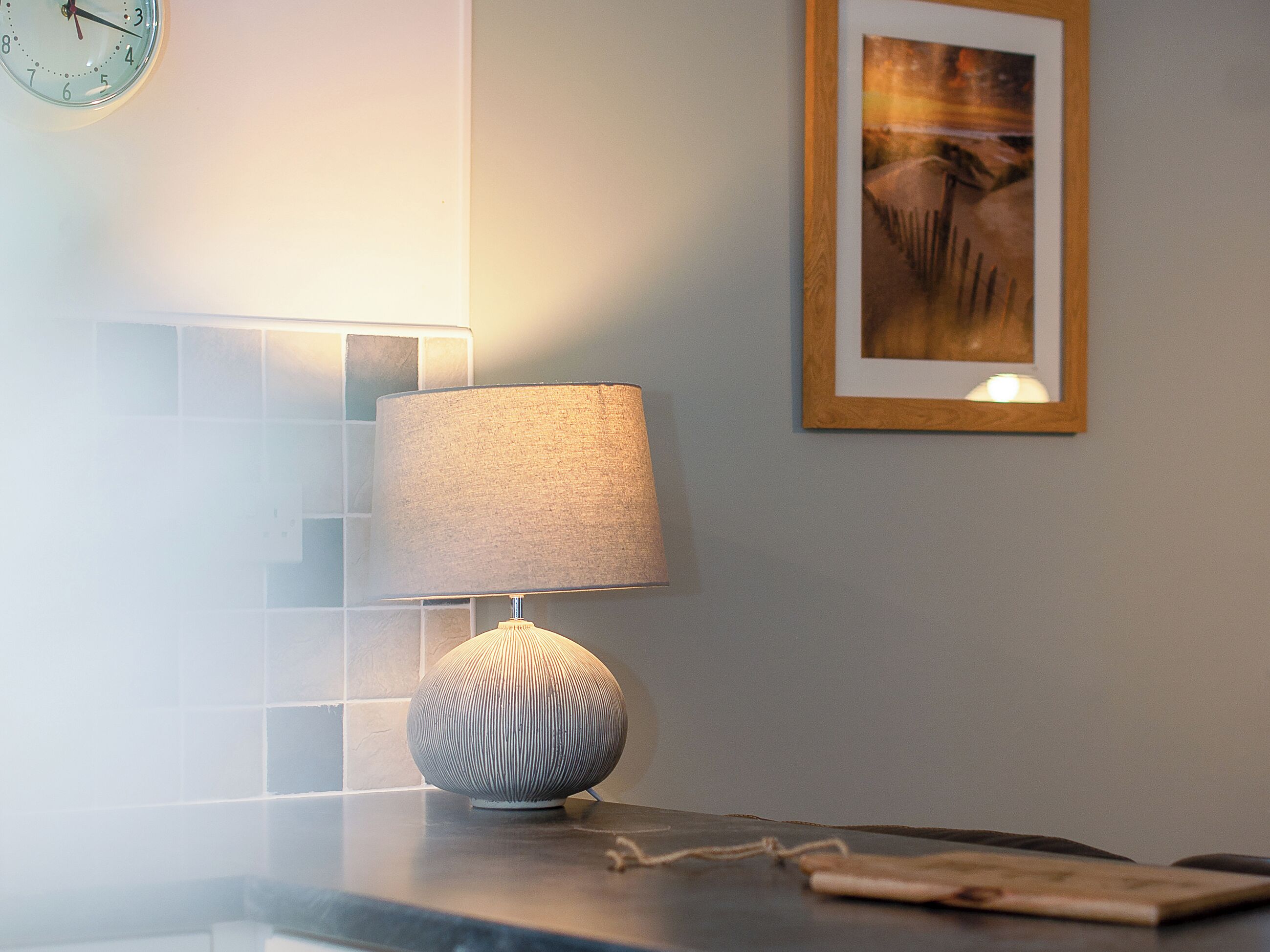 A modern bathroom with a round wall clock, a wall-mounted lamp, and a framed artwork.
