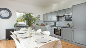 A modern kitchen with grey cabinets, a built-in oven, and a dining area set for six with a star-patterned tablecloth. - Little Dunley Cottages - Apple Lodge (Bovey Tracey)