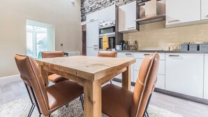 A modern kitchen with white cabinets, a stone accent wall, and a dining area with a wooden table and leather chairs. - 2 bedroom accommodation in Millom, near Haverigg (Millom, near Haverigg)