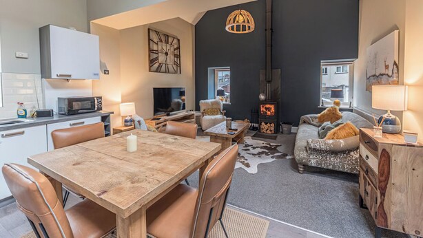 A spacious living area with a high ceiling, a fireplace, a dining table with chairs, and a cozy seating area with cushions. - 2 bedroom accommodation in Millom, near Haverigg (Millom, near Haverigg)