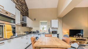 A modern kitchen with white cabinets, a wooden dining table, and leather chairs. - 2 bedroom accommodation in Millom, near Haverigg (Millom, near Haverigg)