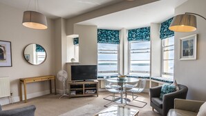 A modern living room with a TV, seating, and large windows overlooking a body of water.
