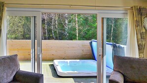 Ein Zimmer mit einer Schiebetür zu einem Außenbereich mit Whirlpool und Holzterrasse. Im Zimmer befinden sich zwei Sofas.