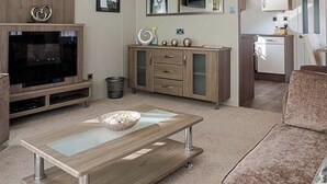 Ein modernes Wohnzimmer mit Flachbildfernseher, einer Holzunterhaltungsecke und einem Essbereich mit Glastisch.