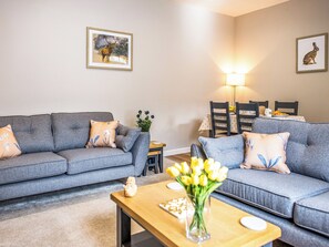 A living room with two grey sofas, a wooden coffee table, a vase of yellow flowers, and framed pictures on the wall.