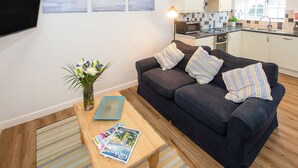 A living room with a dark blue sofa, a wooden coffee table, and a small rug. There is a flat-screen TV mounted on the wall, a vase with flowers, and a magazine on the table. - Number Seven - UKC4969 (Tawstock, near Barnstaple)