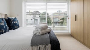 Een slaapkamer met een bed, een bank met handdoeken, een kledingkast en een groot raam met jaloezieën.