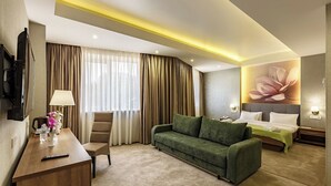 Ein Hotelzimmer mit einem Bett, einem grünen Sofa, einem Holztisch, einem Stuhl und einem Fernseher.
