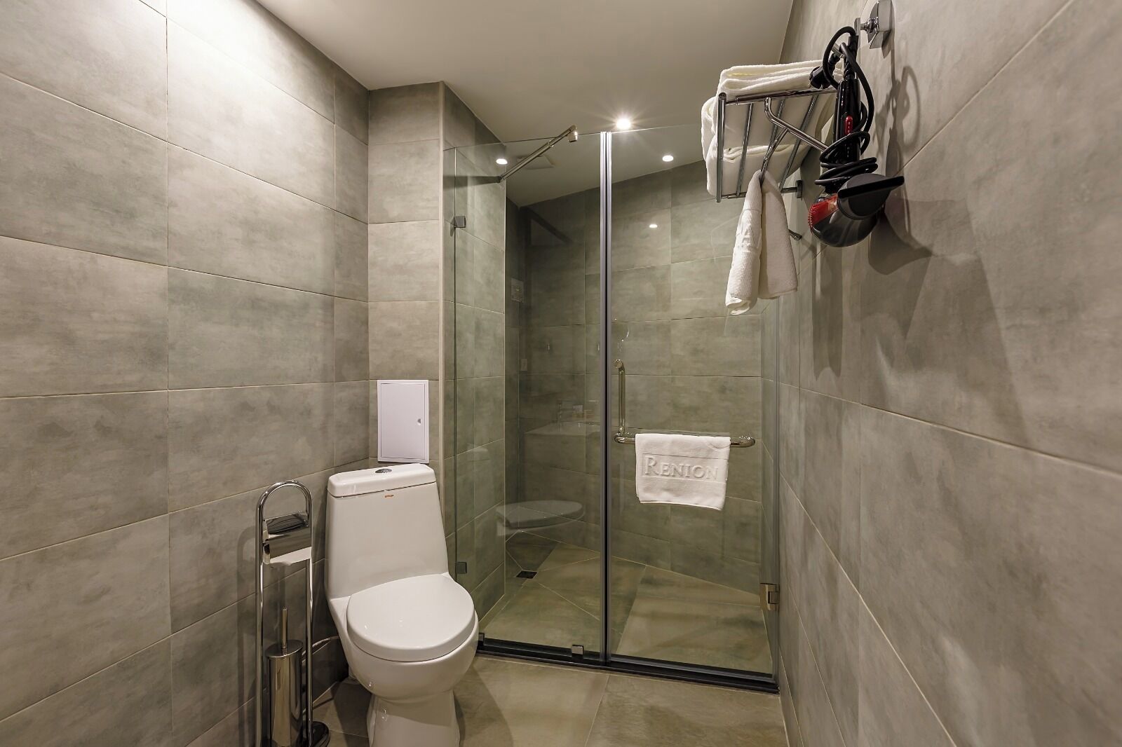 A modern bathroom with a glass shower enclosure, a toilet, and a towel rack with a towel.