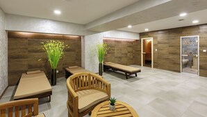 Ein moderner Wellnessraum mit Massageliege, Holzstühlen und Blumentöpfen.