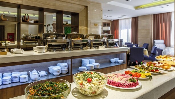 Ein reichhaltiges Buffet mit verschiedenen Speisen, darunter Salate und ein Gericht mit Fleisch, in einem modernen Hotelambiente.