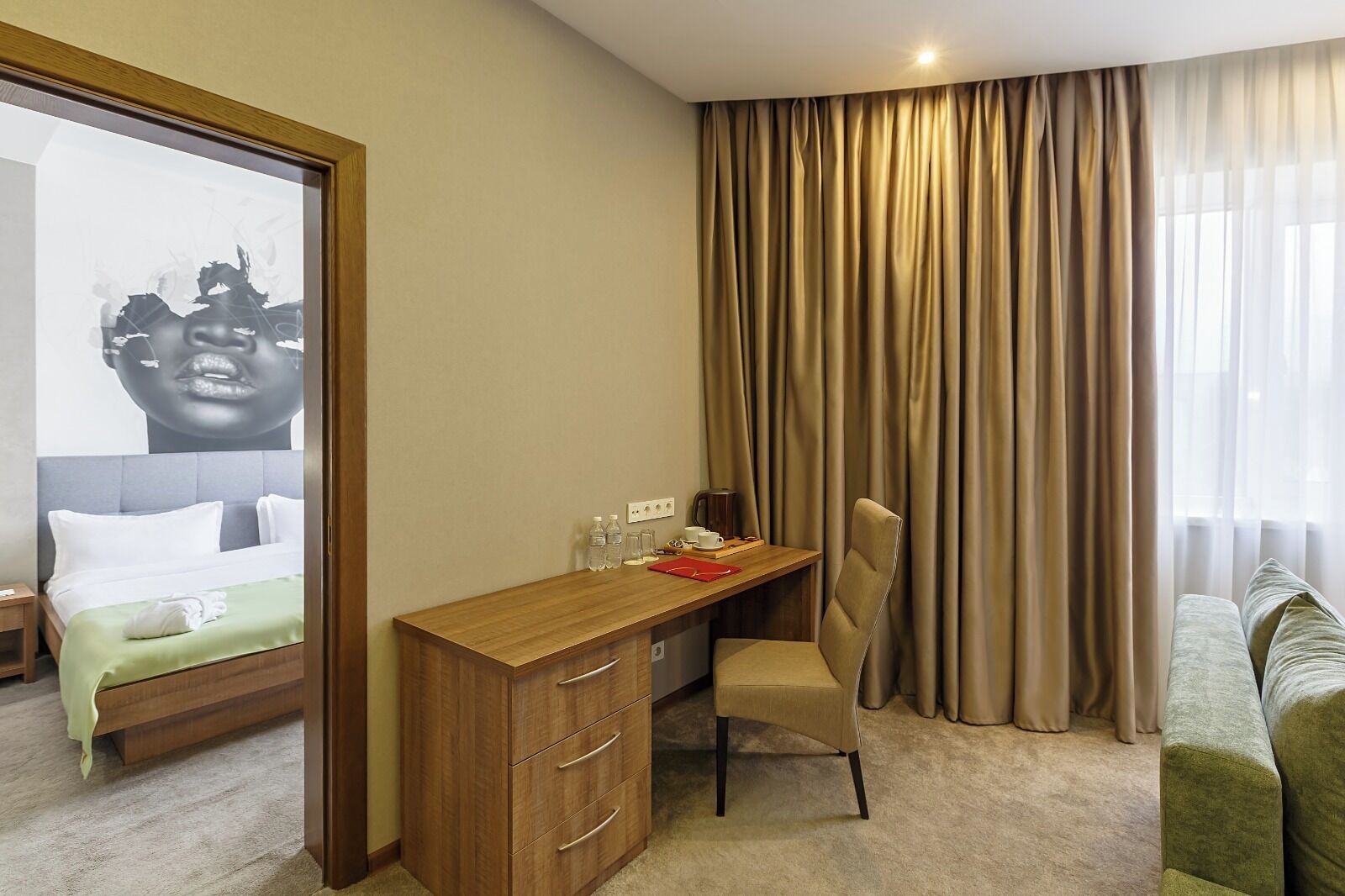 Habitación de hotel con cama, escritorio, silla, armario y un amplio ventanal con cortinas.