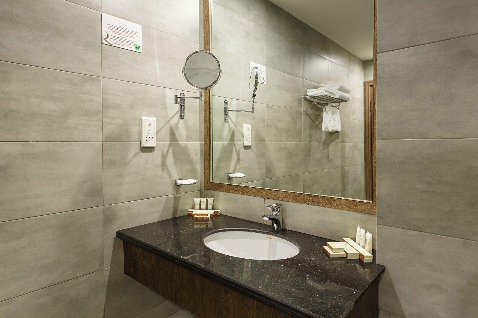 Un baño moderno con un espejo grande, un espejo redondo, un lavamanos con encimera oscura y un perchero con toallas dobladas.