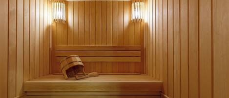 Una sauna con paredes y bancos de madera, un cubo de madera y dos luces fijadas a la pared.