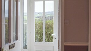 En hvid dør med glasrude, der fører til en balkon med udsigt over grøn vegetation og fjerne bakker.