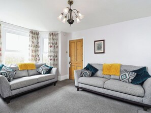 A room with two grey sofas, each with a yellow throw blanket and patterned cushions. A wooden door and a framed picture are on the wall. - 5 bedroom accommodation in Whitwell, Near Ventnor (Whitwell, Near Ventnor)