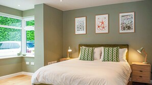A bedroom with a large bed, green patterned pillows, a bedside table with a lamp, and framed artwork on the wall. - 4 bedroom accommodation in Uplyme (Uplyme)