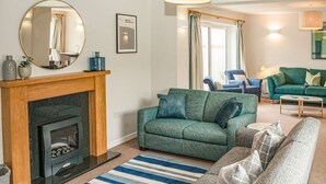 A living room with a fireplace, a green sofa, a blue and white striped rug, and a blue armchair. - 4 bedroom accommodation in Uplyme (Uplyme)