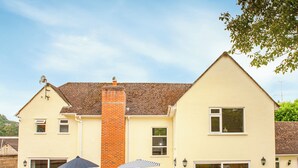 A two-story house with a brick chimney, a patio with chairs and umbrellas, and a large window. - 4 bedroom accommodation in Uplyme (Uplyme)