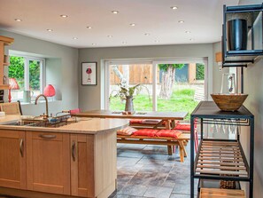 Une cuisine moderne dotée d’un îlot central, de meubles en bois et d’un coin repas avec un banc et des coussins rouges.