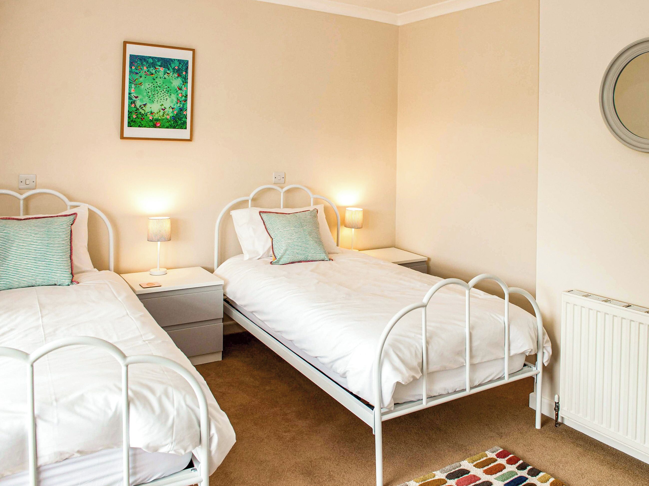 A twin bedroom with two single beds, bedside tables, lamps, a framed picture on the wall, and a radiator.