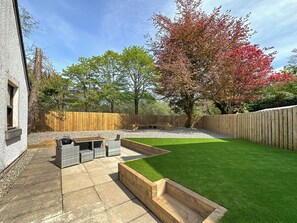 A backyard with a patio, artificial grass, a wooden fence, and trees. - 4 bedroom accommodation in Tarbert (Tarbert)