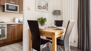 Een moderne keuken met houten kastjes, een magnetron, en een eethoek met een tafel gedekt voor twee personen, stoelen en een potplant.