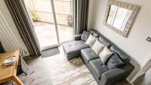 Een moderne woonkamer met een grijze modulaire bank, een houten eettafel met stoelen, en een groot raam met gordijnen.